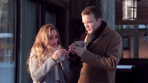 Young happy couple drinking a hot drink on the porch in the winter Stock Footage 72317511