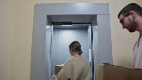 Young happy couple enters in the elevator with cardboard boxes and folding chair Video stock 150097908