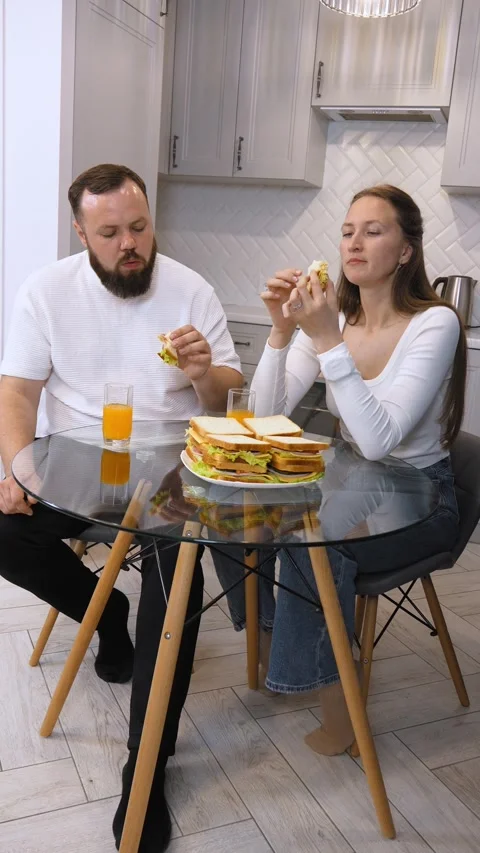 Young happy couple having fun eating sandwiches for breakfast in the kitchen. Stock Footage 320499019
