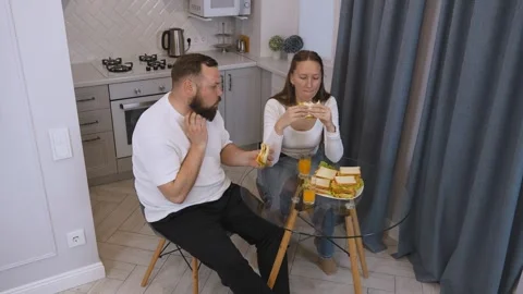 Young happy couple having fun eating sandwiches for breakfast in the kitchen. Stock Footage 320499717