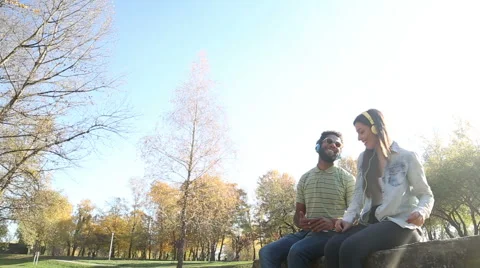 Young happy couple listening to music on headphones at the park Stock Footage 59554750