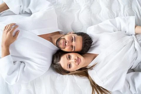 Young happy couple relaxing, lying in bed in white bathrobes, head to head, l 스톡 사진