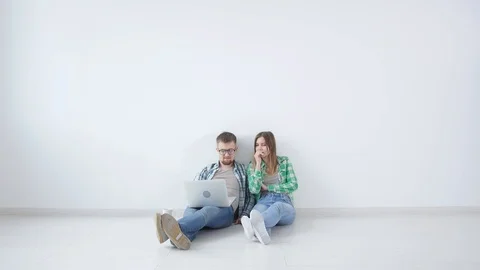 Young happy couple is sitting in an empty room and planning to arrange furniture Stock Footage 111119295