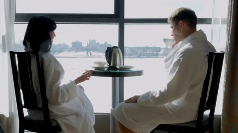 Young happy couple sitting by the window in hotel, at home. A woman and a man Stock Footage 75952948