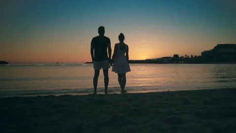 Young happy couple standing on a sandy beach near the sea at sunset, hugging and Stock Footage 104260253