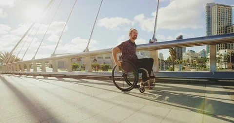 Young happy disabled man pushing wheelchair across bridge in city Stock Footage