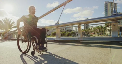 Young happy disabled man pushing wheelchair across bridge in city Stock Footage 96329070
