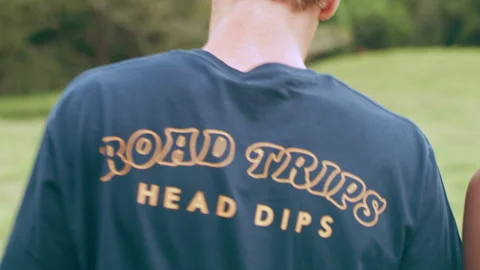 Young, happy, ethnically diverse couple in shorts walk through a field with tree Stock Footage 199455455