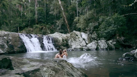 Young, happy, ethnically diverse couple swim and play in stream in front of wate Stock Footage 199458368