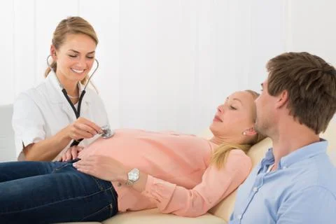 Young Happy Female Doctor Examining Pregnant Woman With Stethoscope In Hospit Stock Photos