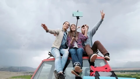 Young happy friends sitting on car outdoors make selfie by phone 20s 4k Stock Footage 79734853