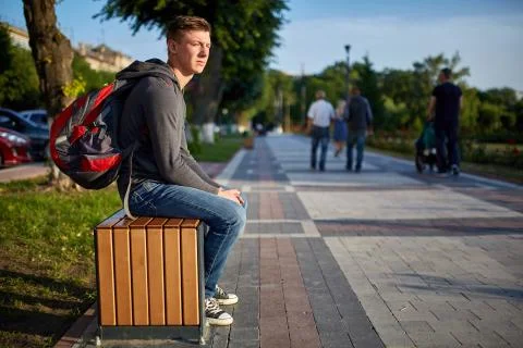A young happy guy with problem skin sitting on the bench while walking around Stock Photos