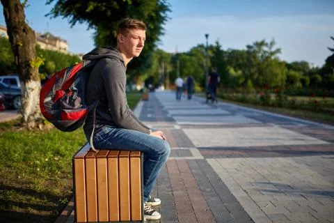 A young happy guy with problem skin sitting on the bench while walking around Stock Photos