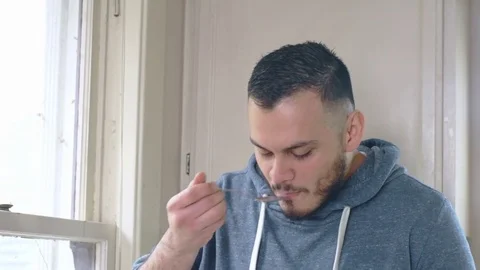 Young happy hispanic man eats cereal while looking out kitchen window Stock Footage 84475108