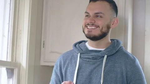 Young happy hispanic man eats cereal while looking out kitchen window Stock Footage 84475202