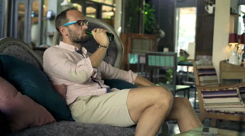 Young, happy man drinking beer sitting on sofa in beautiful, stylish cafe, 4K Stock Footage 68910901