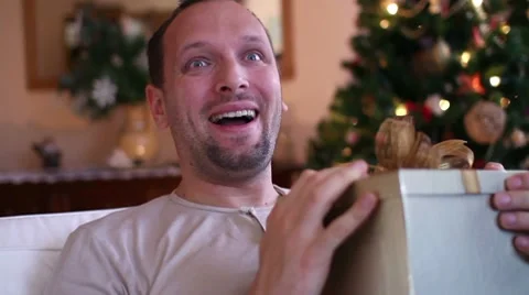 Young happy man gets present, christmas tree in background Stock Footage 10741929