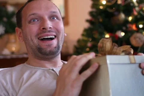 Young happy man gets present, christmas tree in background Stock Footage 10741932