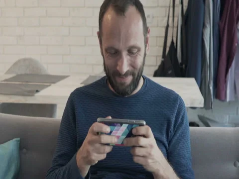 Young, happy man playing game on smartphone on sofa at home Stock Footage 74730652