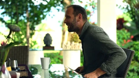 Young, happy man siting at table and drinking tea in the garden, 4K Video stock 76055943