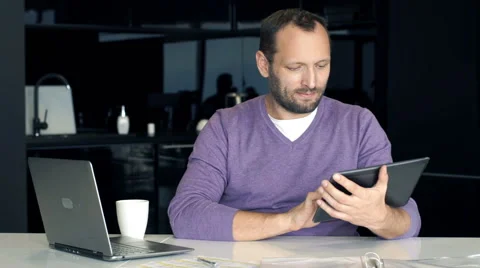 Young happy man sitting with tablet in the kitchen 스톡 동영상 66768261