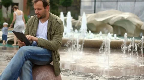 Young happy man with tablet computer sitting by the fountain, slow motion HD Stock Footage 8523963