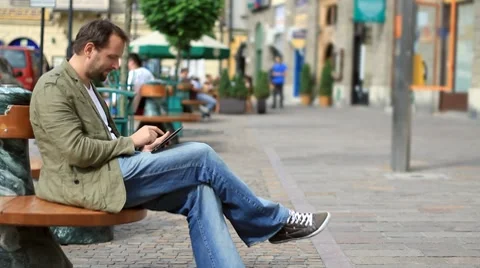 Young happy man with tablet computer sitting in the city HD Stock Footage 8524103
