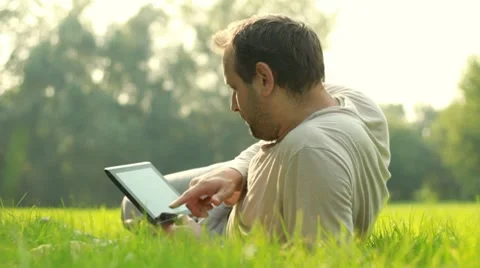 Young happy man with tablet computer lying on the grass Stock Footage 8580434