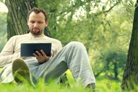 Young happy man with tablet computer by the tree in park, dolly shot Stock Footage 8582254