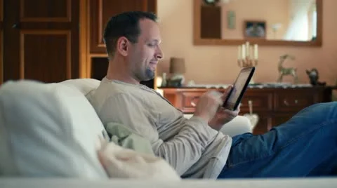 Young happy man with tablet computer sitting on sofa HD Stock-Footage 10592875
