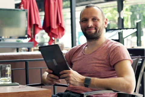 Young happy man with tablet computer sitting in cafe in the city NTSC 스톡 동영상 49413252