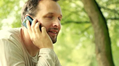 Young happy man talking on mobile phone in the park HD Stock Footage 8573287