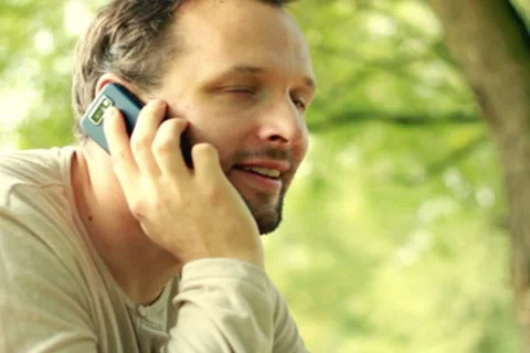 Young happy man talking on mobile phone in the park NTSC Stock Footage 8573297