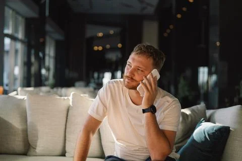 Young happy man using mobile phone in hotel lobby. Stock Photos