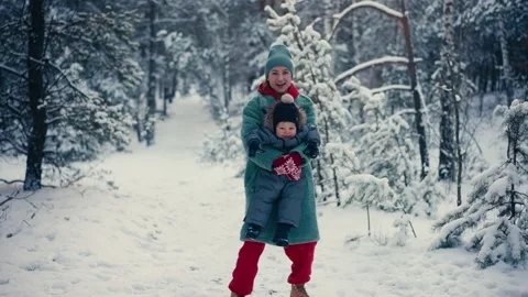 Young happy mother having fun and playing with toddler son in snowy forest in Stock Footage 167995389