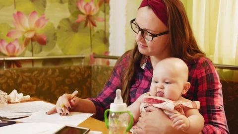 Young happy mother keep her baby and trying to work on laptop with documents Stock Footage 122245673