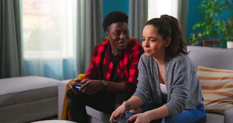 Young happy multinational couple sitting at home on couch and playing video Stockbeeldmateriaal 152348183