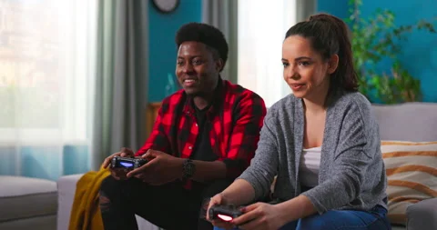 Young happy multinational couple sitting at home on couch and playing video Stockbeeldmateriaal 152348944