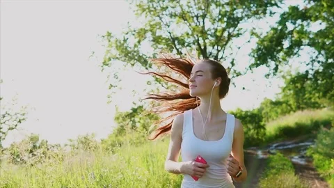 Young happy smiling woman jogging on the nature. She listen to the music. Stock Footage