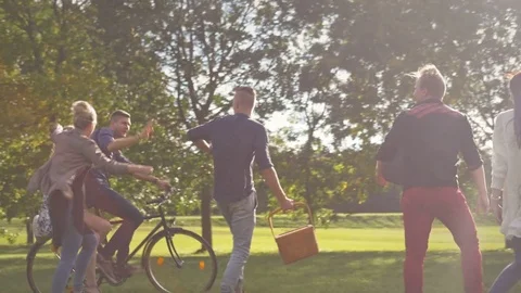 Young happy students walking and riding a bike in park at sunset. Видео 77237017