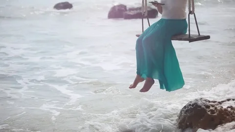 Young happy woman using mobile phone on a swing on a tropical beach and waves Stock Footage
