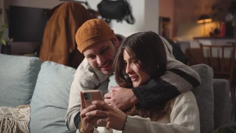 Young heterosexual Hispanic couple embracing on their home sofa while looking at Stock Footage 346162207