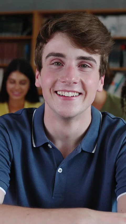 Young high school student boy smiling at camera sitting on chair at library Stock Footage 312198162
