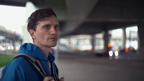 Young hiker dressed in blue jacket with backpack standing under road bridge Stock Footage 80285743