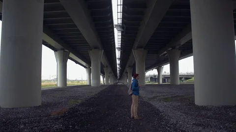 Young hiker dressed in blue jacket with backpack standing under road bridge Stock Footage 80285772