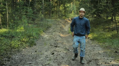 Young hiker man with hat walking in forest. He adjusts his old jeans and goes on Stock Footage 65019410