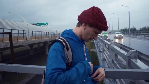 Young hiker using smartphone standing on road bridge. Road highway at background Stock Footage 80286436