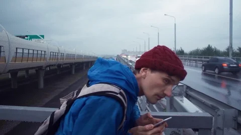 Young hiker using smartphone standing on road bridge. Road highway at background Stock-Footage 80286451