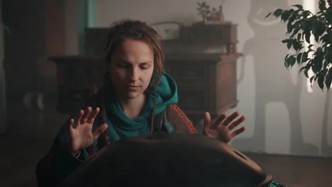 A young hippie with dreadlocks hitting on hangpan with both hands at home. Stock Footage 191039355