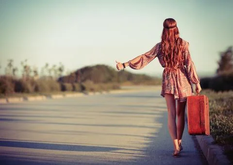 Young hippie woman hitchhiking on the road. Rear view Stock Photos